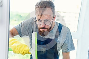 Man as a professional cleaner in blue uniform washing window with rubber brush indoors