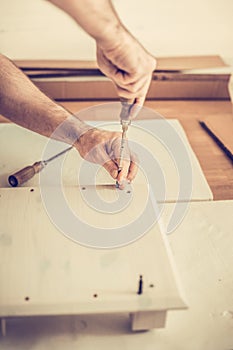 Man assembles furniture wardrobe, twists screws in the slots, furniture assembly