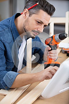 man assembling furniture with electric screwdriver looking at computer