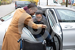 Man Assisting Her Handicapped Wife To Sit On Wheelchair