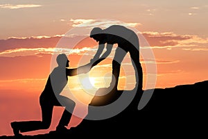 Man Assisting Male Friend In Climbing Rock During Sunset