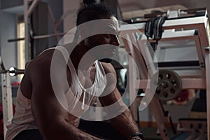 a man athlete with dark skin sits in the gym and looks forward.