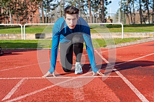 Man athlete on the starting line of a running track at the stadium.