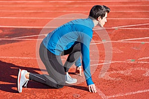 Man athlete on the starting line of a running track at the stadium.
