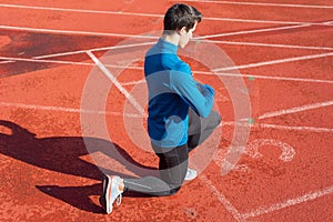 Man athlete on the starting line of a running track at the stadium, resting on his knees.