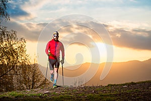 Man athlete with trail beard trail with sticks at sunset