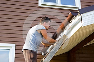 Man attaches gutter on roof of the porch