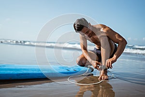 man attaches a safety harness to connect his feet to a surfboard