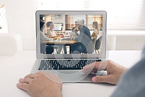 Man attending online video conference via laptop at table