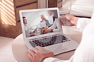 Man attending online video conference via modern laptop at table, closeup