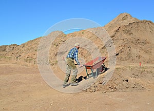 The man of average years is lucky a wheelbarrow with soil on roa