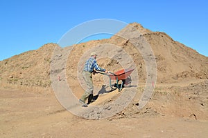 The man of average years is lucky a wheelbarrow with soil on roa