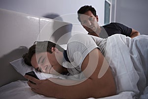 Man awake in bed, while his boyfriend secretly uses phone