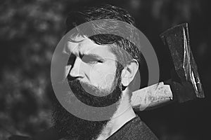 Man with axe outdoor. Handsome man hipster or guy with beard and moustache on serious face.