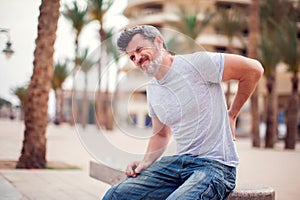 Man with back pain sitting on bench at the outdoor. People, health care and medicine concept