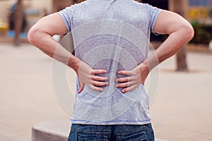 Man with back pain sitting on bench at the outdoor. People, health care and medicine concept