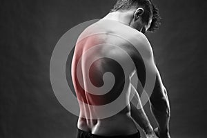 Man with backache. Pain in the human body. Muscular male body. Handsome bodybuilder posing on gray background