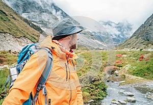 Man with backpack dressed orange waterproof jacket turning back enjoying nature landscape during walking path Makalu Barun