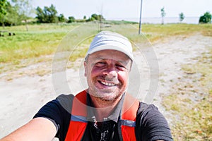 Man with a backpack hikes along a pathway near river beach taking phone selfie photo photo