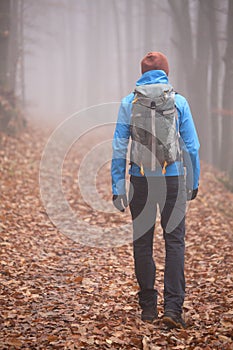 Man with backpack hiking alone in a forest in fall or winter