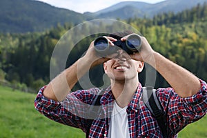 Man with backpack looking through binoculars in mountains