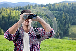 Man with backpack looking through binoculars in mountains