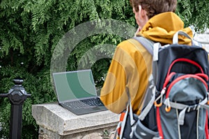 Man with backpack looking at laptop on stone ledge outdoors , symbolizing remote work