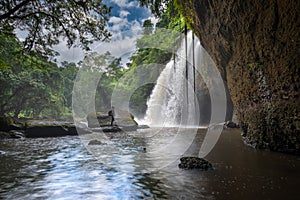 Man with backpack looking at scenic waterfall in Thailand