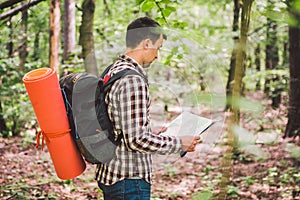 Man with Backpack and map searching directions in wilderness area. Tourist with backpack using map in forest. concept