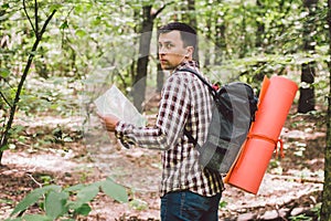 Man with Backpack and map searching directions in wilderness area. Tourist with backpack using map in forest. concept