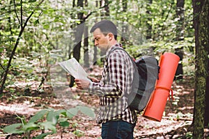 Man with Backpack and map searching directions in wilderness area. Tourist with backpack using map in forest. concept