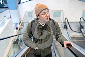 Man with backpack rides escalator in modern shopping mall, dressed casually. Captures urban lifestyle, travel, and photo