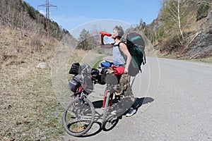 Man with a backpack standing at bicycle and drinking water