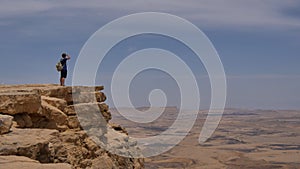 Man with backpack standing on the desert mountain rock cliff edge