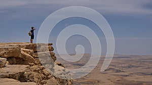Man with backpack standing on the desert mountain rock cliff edge photo