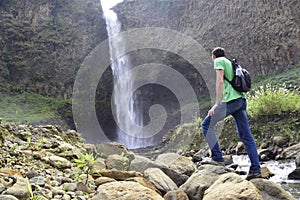 A man with a backpack is standing in front of a waterfall in Banos de Agua Santa, Cascada Manto de la Novia. Banos photo