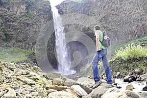 A man with a backpack is standing in front of a waterfall in Banos de Agua Santa, Cascada Manto de la Novia. Banos photo