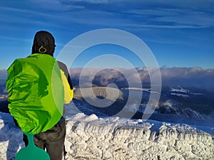 A man with a backpack is standing on the summit of Snezka enjoying beautiful view.