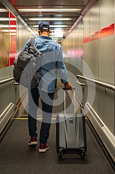 Man With Backpack And Suitcase Walking In Airport Terminal, Rear View Of Young Male On His Way To Flight Boarding Gate