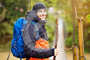 Man with backpack trekking in forest by hinged bridge over river. Cold weathe. Spring hiking. Wooden bridge across the river