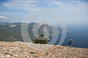 A man with a backpack and trekking poles walking on the edge of a cliff above the sea. Hiking in the mountains high above the sea.