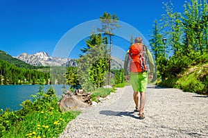 Muž s batohom chodí po horskom chodníku pri jazere
