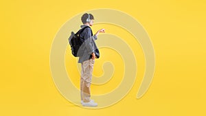 Man With Backpack Wearing Headphones Showing Free Space, Yellow Background