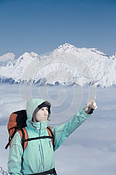 A man with backpack in winter the snowy mountains. Climber stands above the clouds.