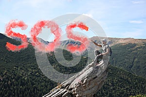 Man with backpack and word SOS made of color smoke bomb on rocky peak
