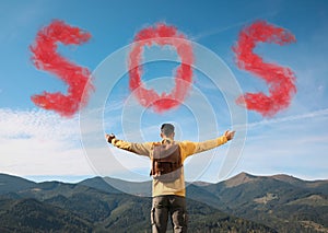 Man with backpack and word SOS made of smoke bomb in mountains, back view