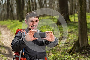 Man backpacker making photo on his camera in forest