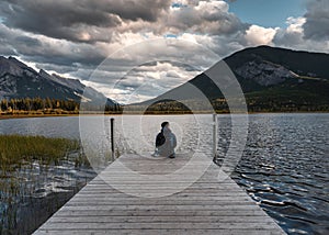 Man backpacker sitting on wooden pier in Vermillion lake at Banff national park