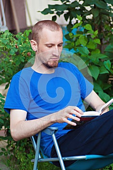 Man at backyard drinking coffee and reading book