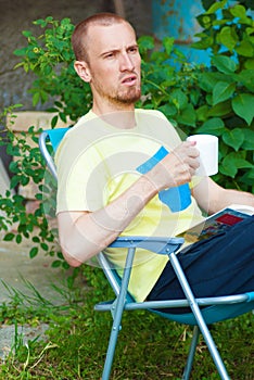 Man at backyard drinking coffee and reading book